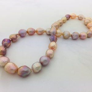 May include: A strand of iridescent freshwater pearls in shades of pink, peach, and lavender. The pearls are irregularly shaped and strung together, creating a unique and elegant necklace or bracelet.