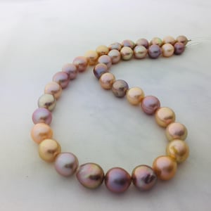 以下が含まれることがあります： 虹色のマルチカラーパールネックレス。 ピーチとゴールドからラベンダーとディープパープルへと変化するパール。 パールは丸く、滑らかで光沢のある表面を持っています。 ネックレスは細い透明なコードに通されています。