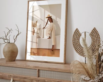 May include: A framed art print featuring a figure in a straw hat and cream-colored clothing, posed on a white structure. The artwork is set against a backdrop of soft shadows and warm tones, with a vase and decorative elements visible.