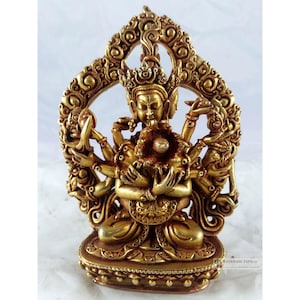 May include: A gold-coloured metal statue of a deity with multiple arms holding a sphere. The statue is sitting on a base with intricate details.