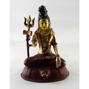 May include: A gold and red painted statue of Shiva, a Hindu deity, sitting in a meditative pose. He is holding a trident in his right hand and has a third eye on his forehead.