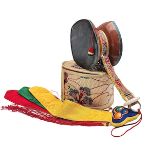 Puede incluir: Un tambor damaru tibetano tradicional con una caja cilíndrica y cintas de seda coloridas. El tambor tiene una cabeza gris oscuro y un cuerpo de madera. La caja es beige con motivos florales.