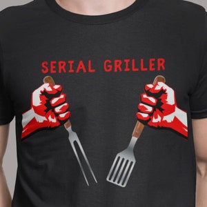 A man with his hands in his pockets wearing a shirt that says "Serial Griller" with two hands holding a grill fork and a spatula.