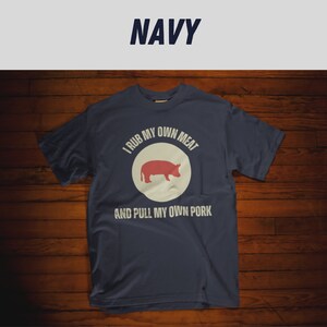 May include: A navy blue t-shirt with a white circle and a red pig silhouette. The text "I rub my own meat and pull my own pork" is printed on the shirt.
