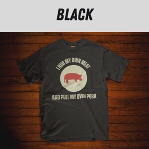 May include: A dark gray t-shirt with a white circle and a red pig silhouette. The text "I rub my own meat and pull my own pork" is printed on the shirt.
