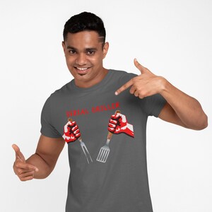 May include: A dark gray t-shirt with the text "SERIAL GRILLER" in red letters. Two red hands are holding a spatula and a fork.
