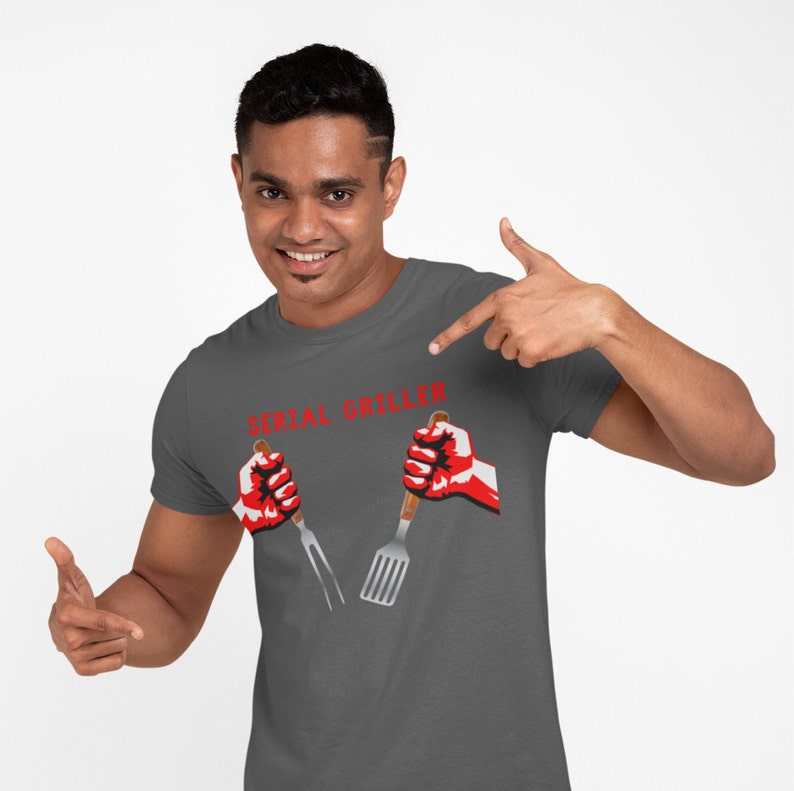 May include: A dark gray t-shirt with the text "SERIAL GRILLER" in red letters. Two red hands are holding a spatula and a fork.