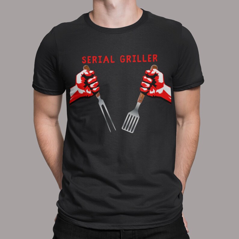 A man with his hands in his pockets wearing a shirt that says "Serial Griller" with two hands holding a grill fork and a spatula.