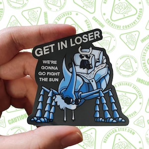 Puede incluir: Una pegatina con una ilustración azul y negra de una criatura parecida a un escarabajo y el texto "GET IN LOSER, WE'RE GONNA GO FIGHT THE SUN." La pegatina tiene un fondo blanco con diseños triangulares verdes repetidos.