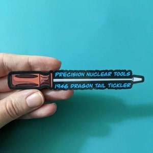 May include: A black and white sticker with a cartoon illustration of a screwdriver. The text on the sticker reads "PRECISION NUCLEAR TOOLS 1946 DRAGON TAIL TICKLER".