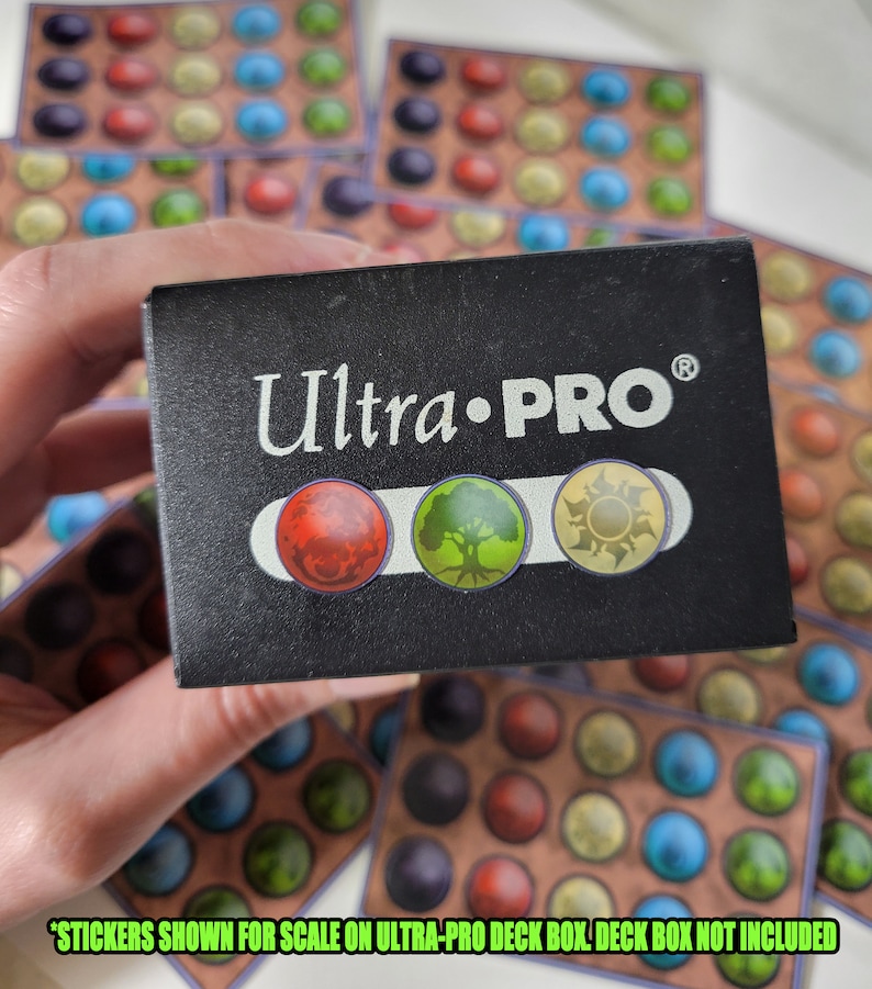 May include: A black Ultra-PRO deck box with a silver logo and three colored circles. The circles are red, green, and yellow. The text "Ultra-PRO&reg;" is printed on the box. "STICKERS SHOWN FOR SCALE ON ULTRA-PRO DECK BOX. DECK BOX NOT INCLUDED" is printed below the circles.