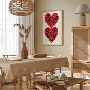 以下が含まれることがあります： 木製のテーブルと椅子、茶色のテーブルクロス、籐製の照明器具が天井から吊り下げられているダイニングルーム。壁には、黒い線で描かれた2つの赤いハートの絵が額縁に入っています。背景には、籐製のドアが付いた木製のキャビネットがあります。