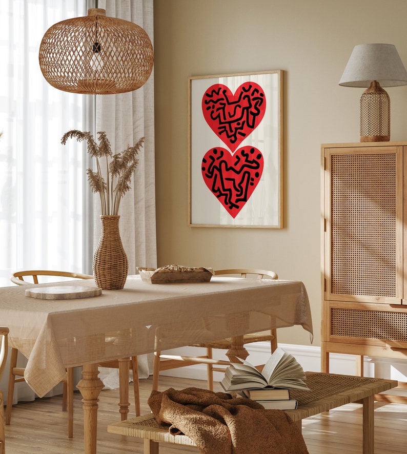 以下が含まれることがあります： 木製のテーブルと椅子、茶色のテーブルクロス、籐製の照明器具が天井から吊り下げられているダイニングルーム。壁には、黒い線で描かれた2つの赤いハートの絵が額縁に入っています。背景には、籐製のドアが付いた木製のキャビネットがあります。