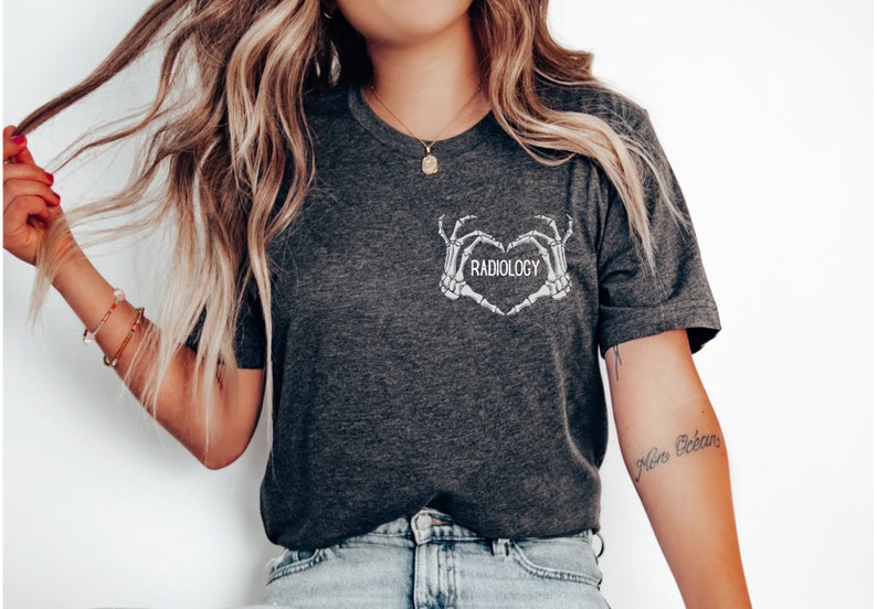 Op de afbeelding: Een donkergrijs T-shirt met een witte afbeelding van twee skelethandjes die een hart vormen met het woord "RADIOLOGY" erin.