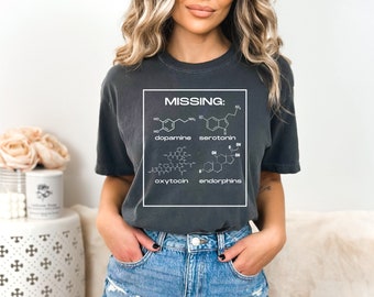 May include: A grey t-shirt with a white graphic that says "MISSING:" and shows the chemical structures of dopamine, serotonin, oxytocin, and endorphins.