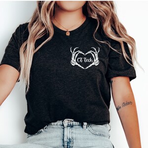 Könnte beinhalten: Ein dunkelgraues T-Shirt mit einer weißen Grafik von Skeletthänden, die eine Herzform mit dem Text "CT Tech" bilden.