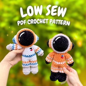 May include: Two crocheted astronaut dolls featuring black helmets with white highlights. One doll has a white suit with orange and blue accents, while the other has an orange suit with white and black accents. Text reads LOW SEW PDF CROCHET PATTERN.