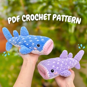 May include: Two crocheted whale shark plushies, one blue and one purple, are held up against a blurred green background. The blue shark has white spots and a pink mouth. The purple shark has white spots and a pink mouth. The text "PDF CROCHET PATTERN" is at the top.