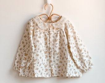 Cream cotton blouse with flower print for babies and girls. Peter pan collar with lace. Button closure in front. Sleeves with elastic cuffs.