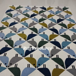 May include: A white rug with a geometric pattern of blue, green, gray, and yellow birds. The birds are arranged in a repeating pattern of triangles.
