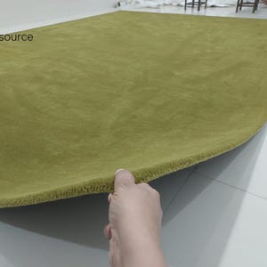 K&ouml;nnte beinhalten: Ein einfarbiger, olivgr&uuml;ner, rechteckiger Teppich mit einer kurzen, dichten Florstruktur. Der Teppich ist an einer Ecke angehoben, um die Dicke und die eingefasste Kante zu zeigen. Der Text RugResource ist oben links in Schwarz aufgedruckt.