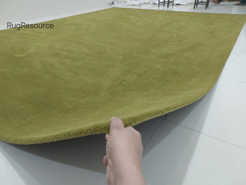 K&ouml;nnte beinhalten: Ein einfarbiger, olivgr&uuml;ner, rechteckiger Teppich mit einer kurzen, dichten Florstruktur. Der Teppich ist an einer Ecke angehoben, um die Dicke und die eingefasste Kante zu zeigen. Der Text RugResource ist oben links in Schwarz aufgedruckt.