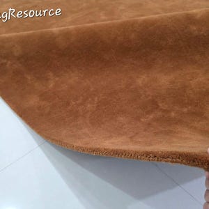 K&ouml;nnte beinhalten: Ein einfarbiger brauner Teppich mit einer dichten Kurzflor-Struktur. Der Teppich ist umgeklappt, um seine Dicke und Beschaffenheit zu zeigen. Der Text "RugResource" ist in Wei&szlig; in der oberen linken Ecke des Bildes aufgedruckt.