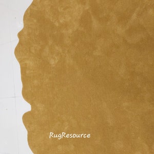 May include: A close-up of a mustard yellow shag rug with an irregular, organic shape. The rug is on a white tiled floor. The text "RugResource" is visible in the lower right corner of the image.
