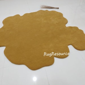 May include: A large, mustard yellow, irregularly shaped rug with a soft, fluffy texture. The rug is made of a plush material and has a unique, organic shape. The text "RugResource" is printed in white on the rug.