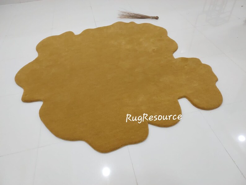 May include: A large, mustard yellow, irregularly shaped rug with a soft, fluffy texture. The rug is made of a plush material and has a unique, organic shape. The text "RugResource" is printed in white on the rug.