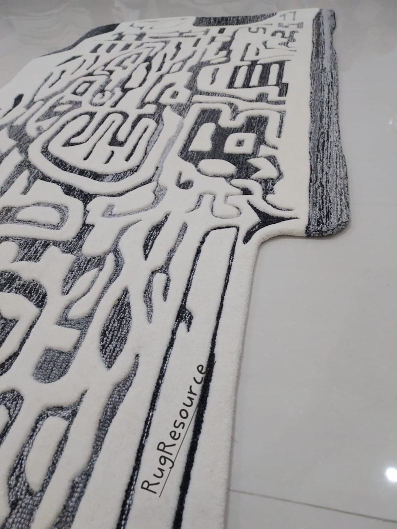 May include: A white and gray abstract patterned rug with a black border. The rug has a unique design with a textured surface. The text "RugResource" is printed on the rug.