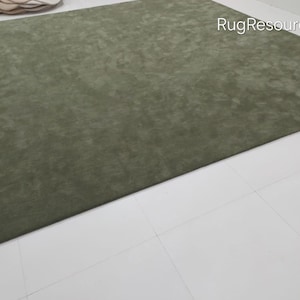 May include: A large, rectangular olive green rug. The rug has a soft, textured appearance and is placed on a white tiled floor. The words "RugResource" are visible in the upper right corner. The rug is a solid color and appears to be made of a plush material.
