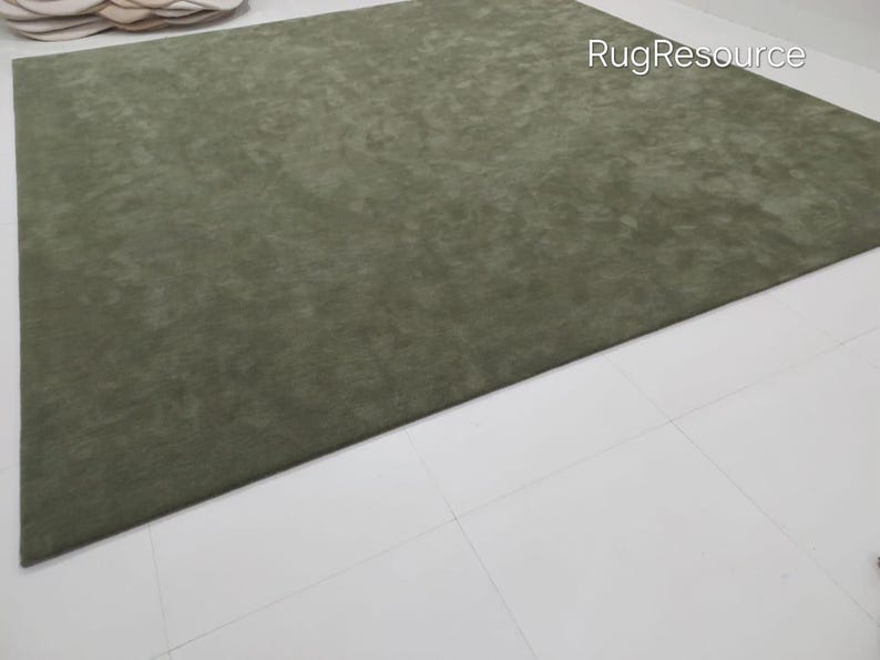 May include: A large, rectangular olive green rug. The rug has a soft, textured appearance and is placed on a white tiled floor. The words "RugResource" are visible in the upper right corner. The rug is a solid color and appears to be made of a plush material.