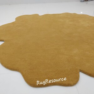 May include: A large, mustard yellow, cloud-shaped rug with a slightly irregular shape. The rug is made of a soft, plush material and has a subtle texture. The text "RugResource" is printed in white on the rug.