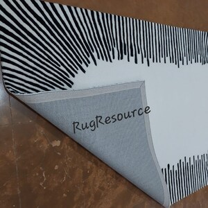 May include: Black and white striped rug with a large white circle in the center. The rug is folded in half, showing the gray backing. The text "RugResource" is visible on the backing.