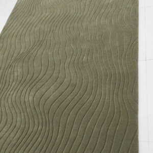 May include: A green rug with a wavy pattern. The rug is made of a soft, plush material and has a subtle sheen. The rug is perfect for adding a touch of elegance to any room.