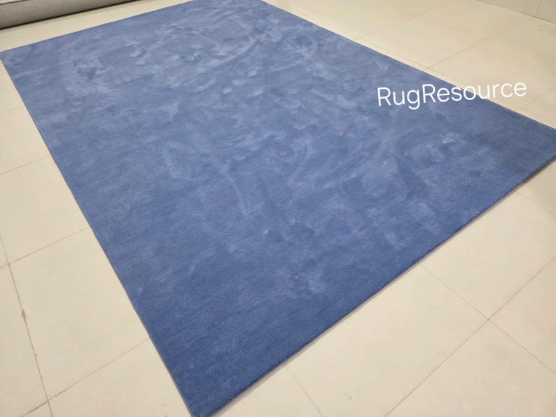May include: A large, rectangular, solid blue rug. The rug has a soft, textured appearance and is placed on a light-colored tiled floor. The text "RugResource" is visible in the upper right corner.
