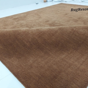 May include: A large, rectangular brown rug with a soft, plush texture. The rug is folded over, revealing the underside. The words "RugResource" are visible on the rug's surface.