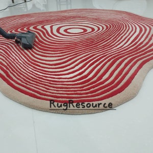 May include: A red and white striped rug with a wavy, organic shape. The rug has a concentric circle pattern in the center.