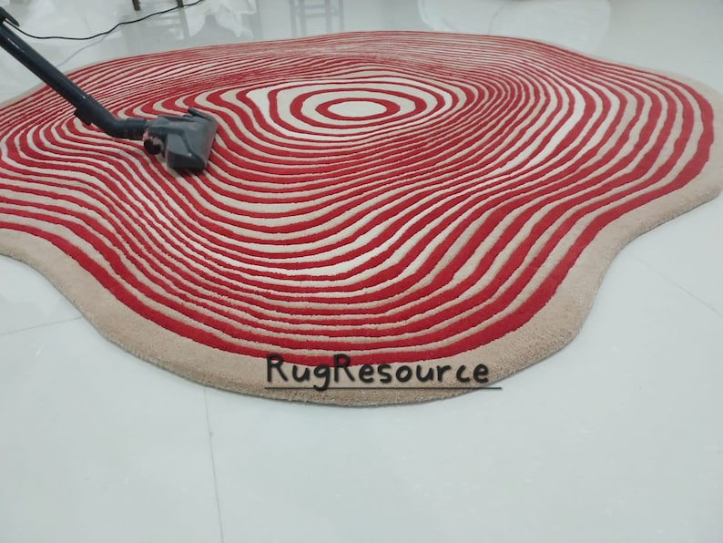 May include: A red and white striped rug with a wavy, organic shape. The rug has a concentric circle pattern in the center.