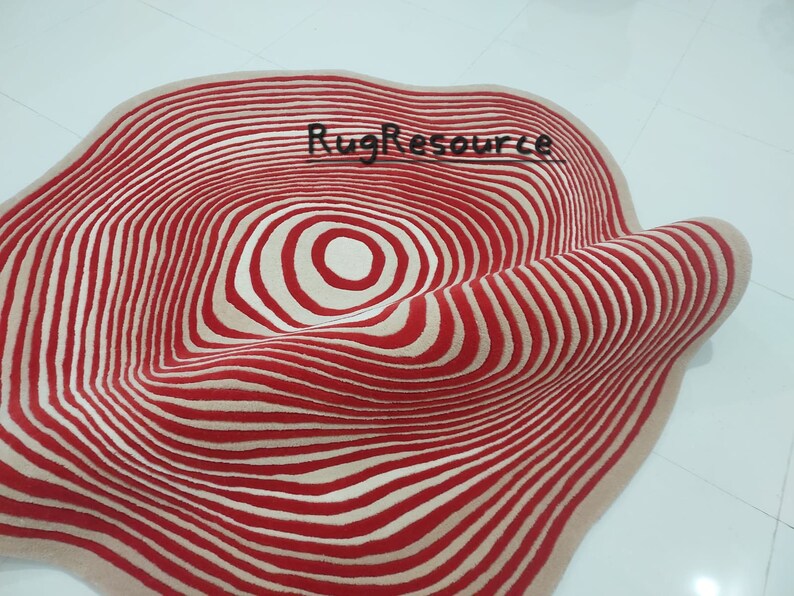 May include: A red and cream colored rug with a circular pattern of concentric circles. The rug is made of wool and has a soft, plush texture.