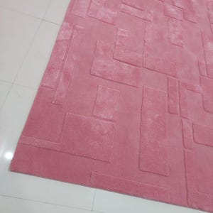 May include: A pink area rug with a geometric pattern. The rug has a raised, textured design.