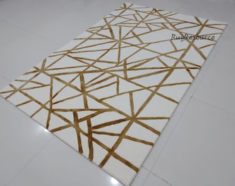 May include: White area rug with a geometric pattern of gold lines forming triangles and other shapes. The rug has a modern design and would be a great addition to any contemporary home.