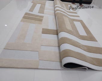 May include: A white and beige area rug with a geometric pattern. The rug is rolled up and the edge of the rug is visible.