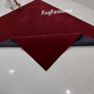May include: A red carpet with a gray backing is folded in half. The carpet is on a white tiled floor. The text "RugResource" is visible in the upper right corner of the image.