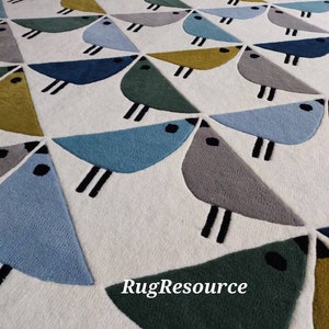 May include: A white rug with a geometric pattern of blue, green, gray, and yellow birds. The rug has a modern design and is perfect for a living room or bedroom.