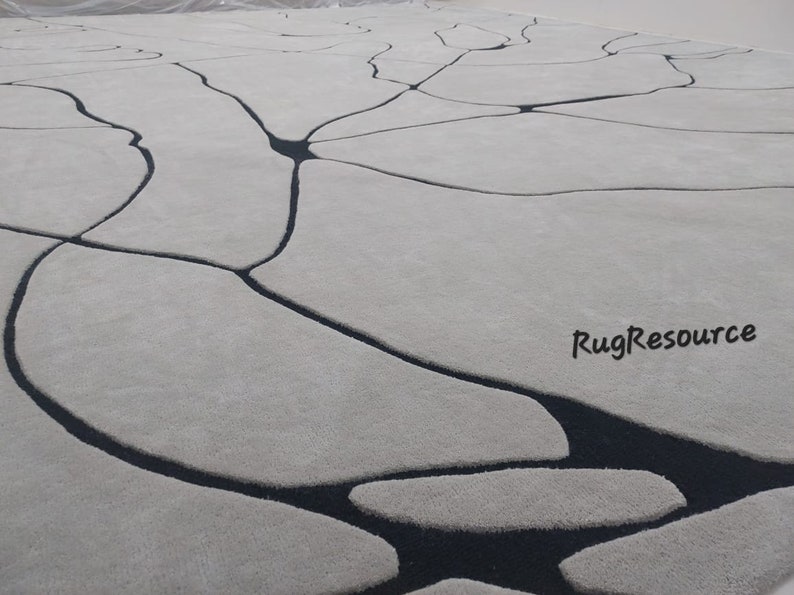 Puede incluir: Una alfombra blanca con un dise&ntilde;o abstracto negro. El dise&ntilde;o se asemeja a una red de venas o grietas. La alfombra tiene una textura suave y mullida. RugResource est&aacute; impreso en la esquina inferior derecha.