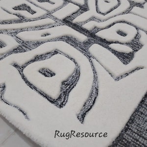 May include: White and gray area rug with a modern abstract design. The rug has a raised texture and a border of gray.
