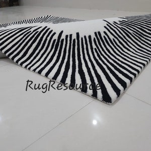 May include: Black and white striped rug with a circular pattern. The rug is made of a soft, plush material and has a modern design.