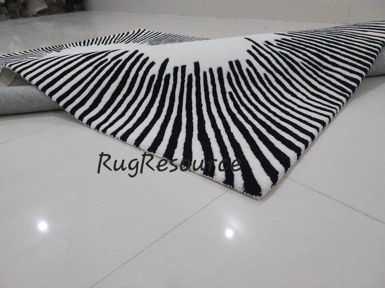 May include: Black and white striped rug with a circular pattern. The rug is made of a soft, plush material and has a modern design.